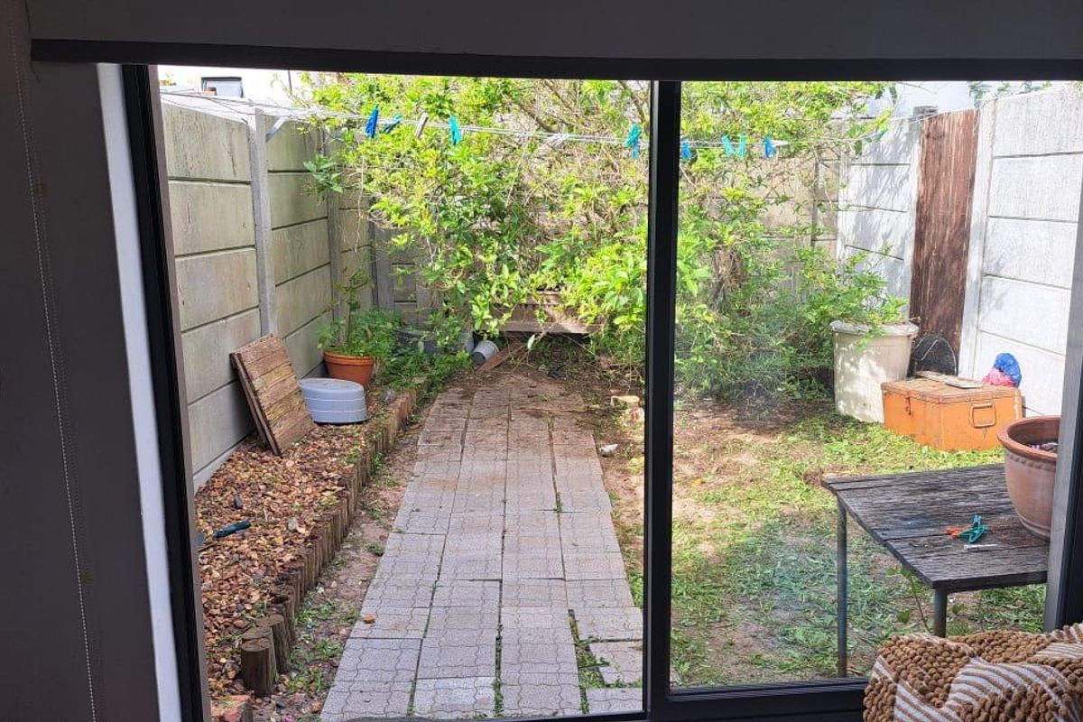 View from an interior sliding door looking out onto a rear garden area with a paved path and perimeter concrete walling.
