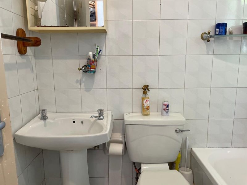 A functional bathroom featuring a pedestal washbasin, toilet, and bathtub with white wall tiling throughout.