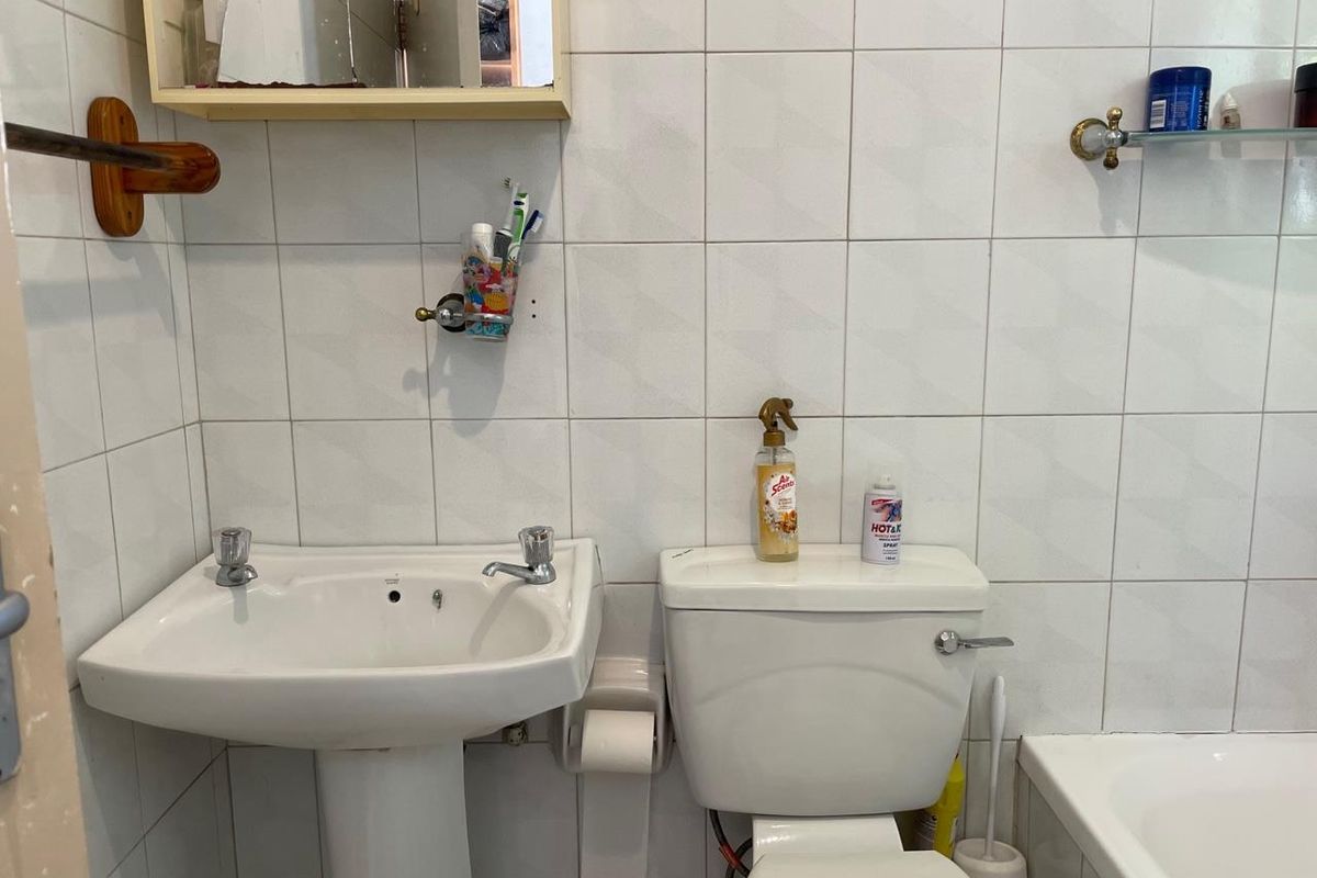 A functional bathroom featuring a pedestal washbasin, toilet, and bathtub with white wall tiling throughout.