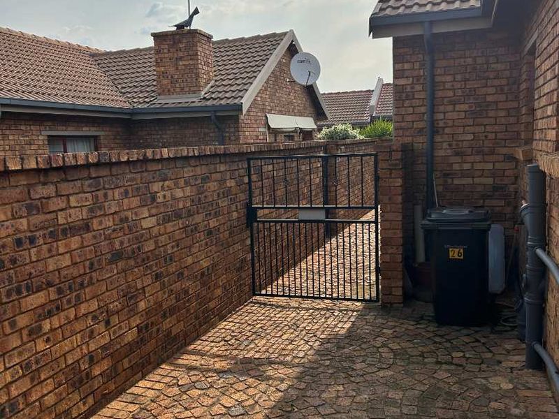A private rear courtyard area featuring durable cobblestone paving, a brick boundary wall, and a secure metal gate access point.