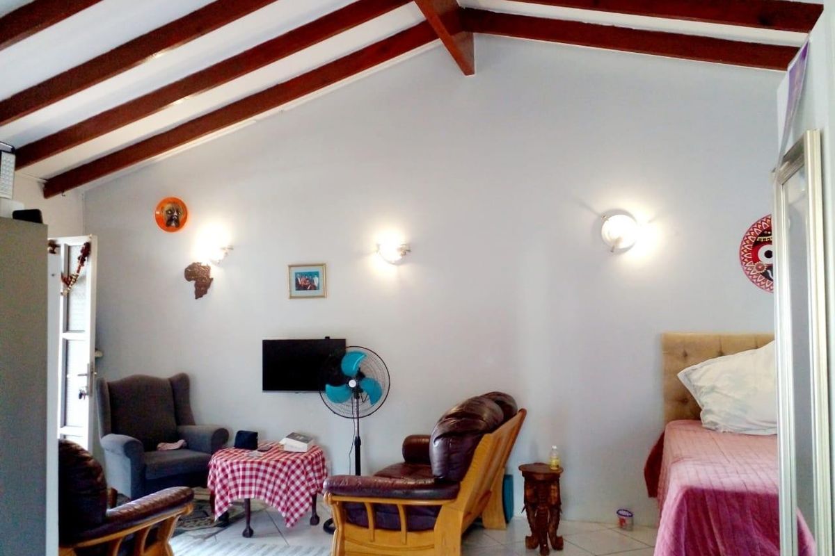 Spacious bedroom featuring high vaulted ceilings with exposed timber beams, tiled flooring, and wall-mounted lighting.