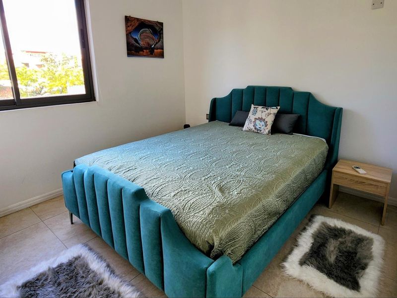 A well-lit bedroom featuring neutral tiled flooring and a large window, providing a clean and functional space.
