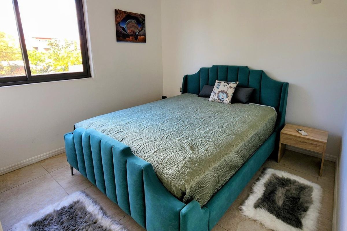 A well-lit bedroom featuring neutral tiled flooring and a large window, providing a clean and functional space.