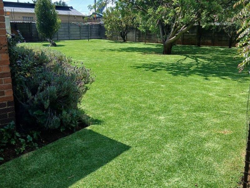 A well-maintained, spacious private garden featuring a lush green lawn, mature trees, and secure precast concrete boundary walls.