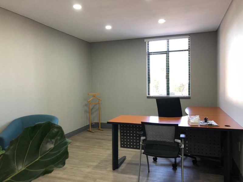 A well-maintained office space featuring neutral wall tones, recessed downlighting, laminate flooring, and a large window with venetian blinds.