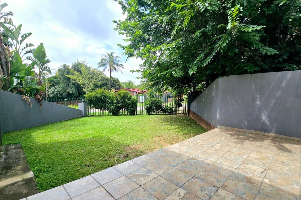 A private rear garden featuring a paved patio area, well-maintained lawn, and perimeter boundary walls with metal fencing.