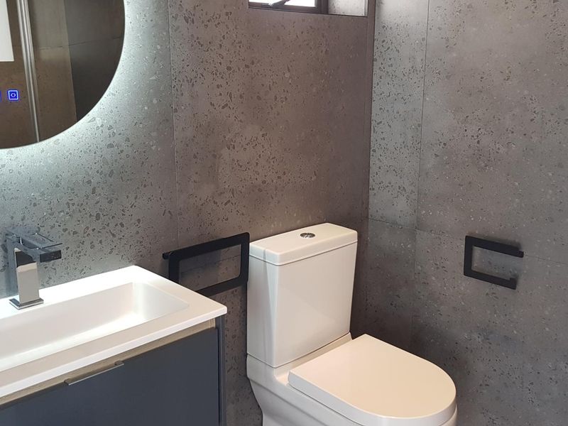 Modern bathroom featuring contemporary grey terrazzo-style wall tiles, a sleek vanity with integrated basin, and a stylish LED backlit mirror.