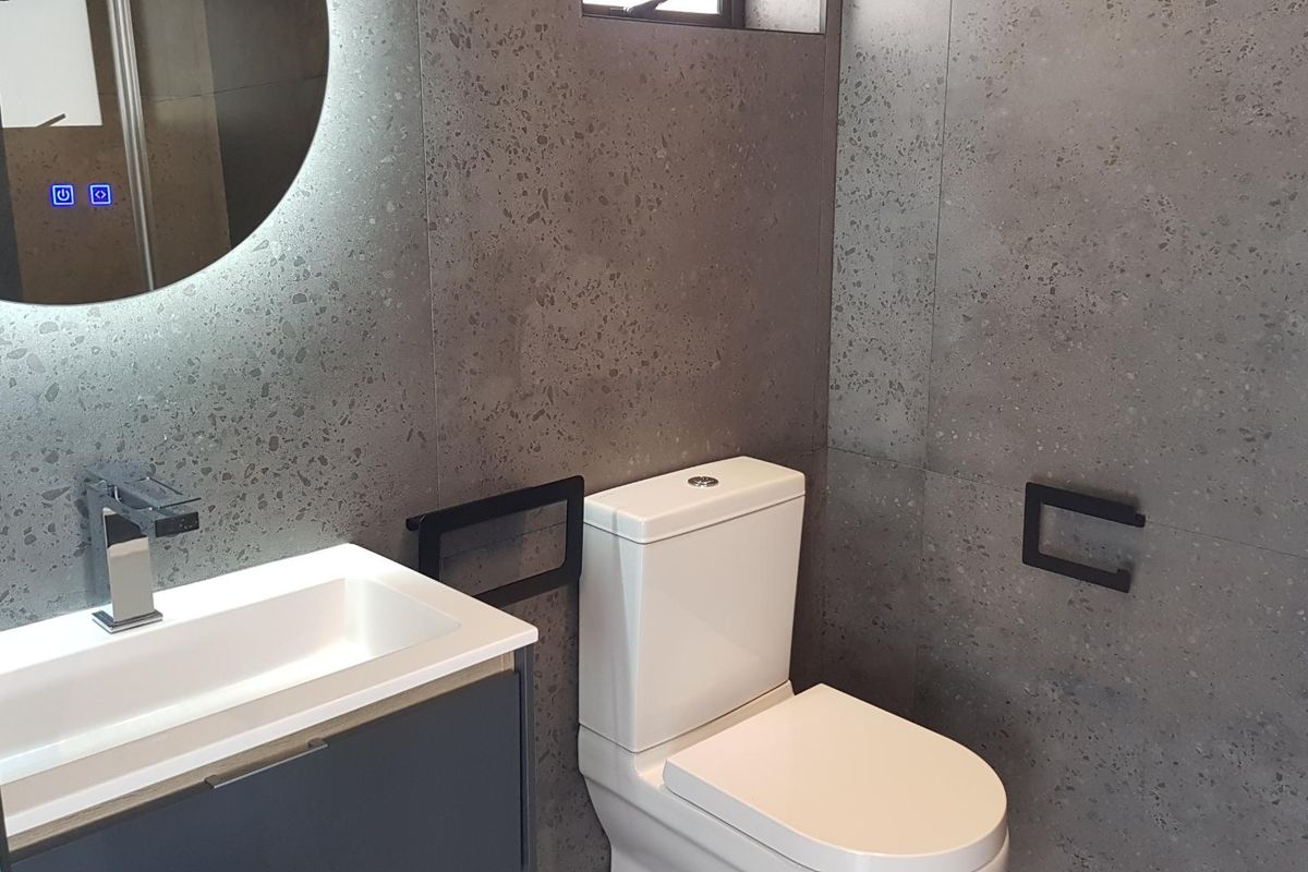 Modern bathroom featuring contemporary grey terrazzo-style wall tiles, a sleek vanity with integrated basin, and a stylish LED backlit mirror.