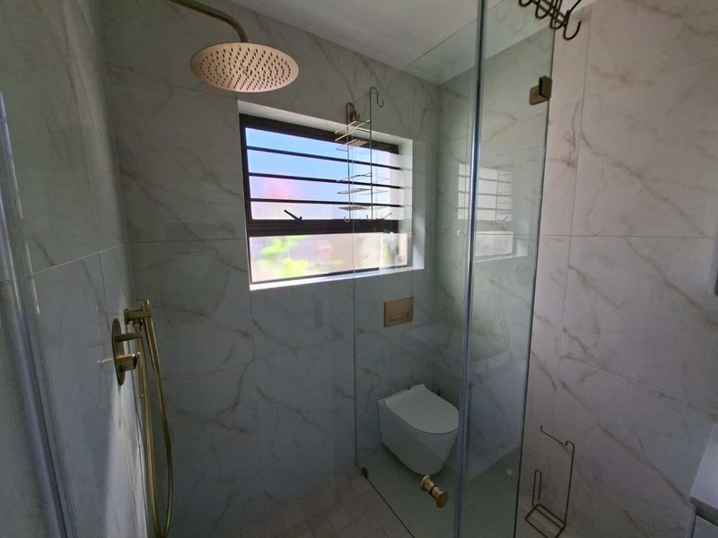 Modern bathroom featuring marble-look wall tiles, a glass-enclosed shower with brass fixtures, and a wall-mounted toilet.