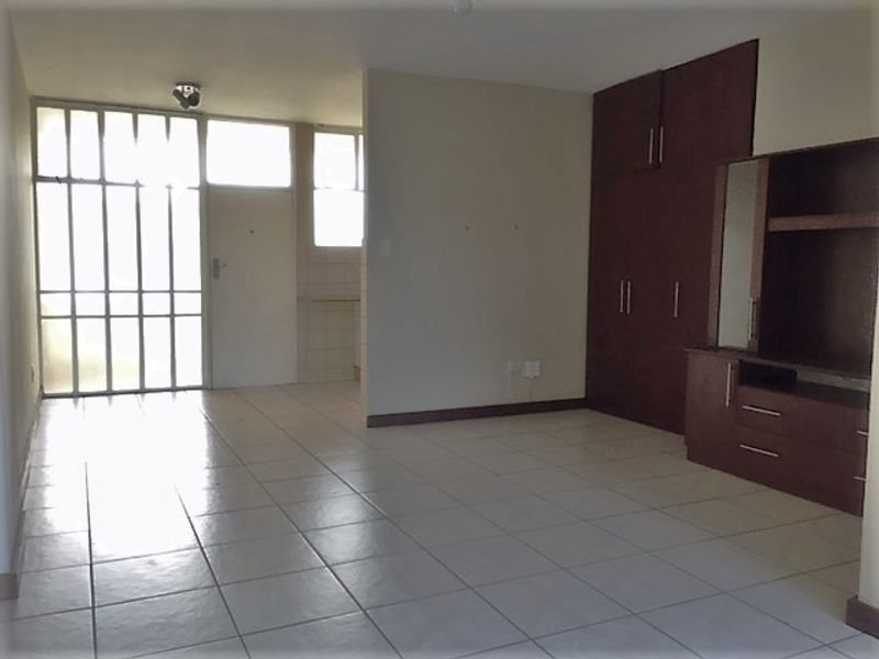 An open-plan living area featuring tiled flooring, built-in storage cabinetry, and a secure entrance with a metal security gate.
