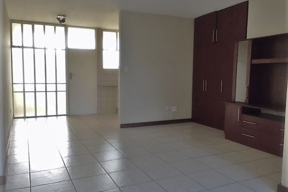 An open-plan living area featuring tiled flooring, built-in storage cabinetry, and a secure entrance with a metal security gate.