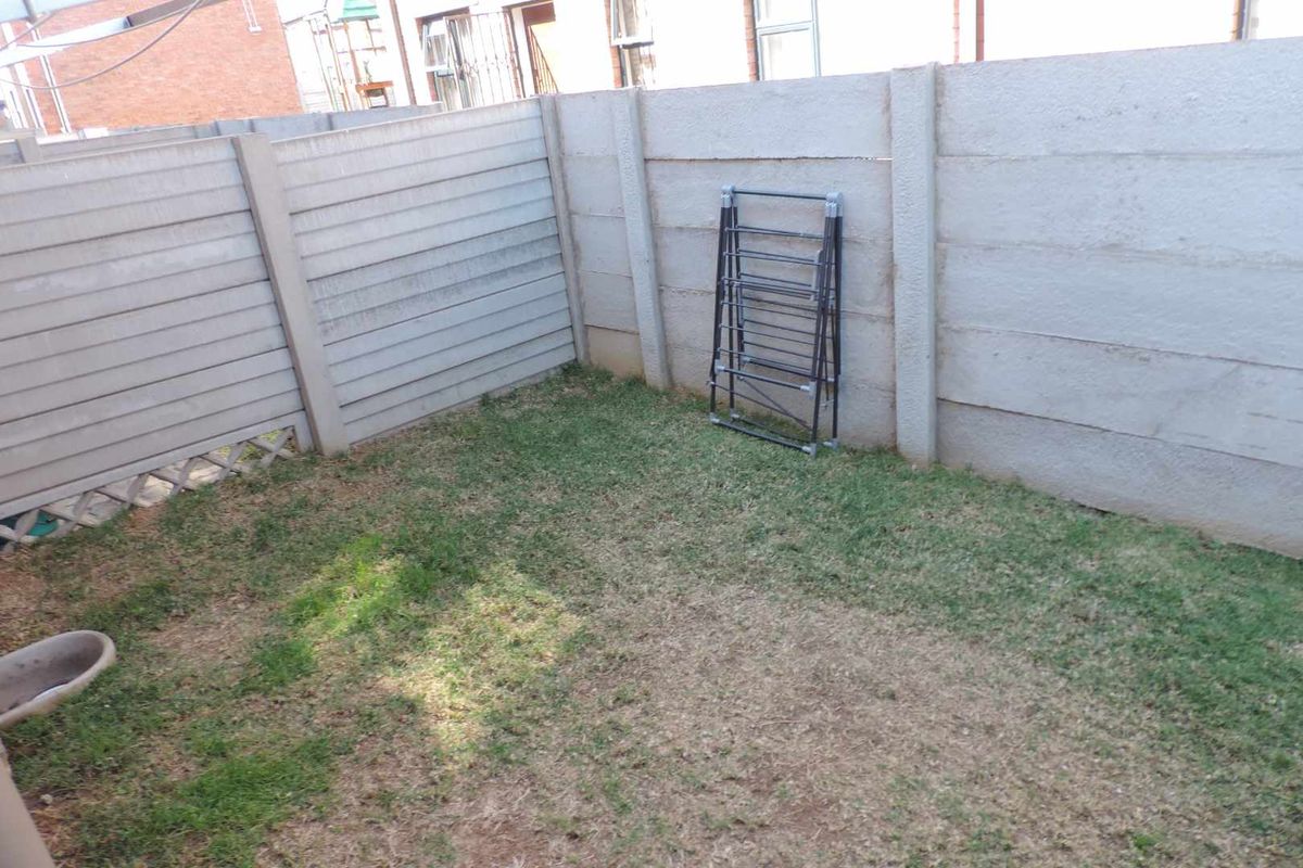 A small, private rear courtyard featuring a lawn area enclosed by precast concrete boundary walls.