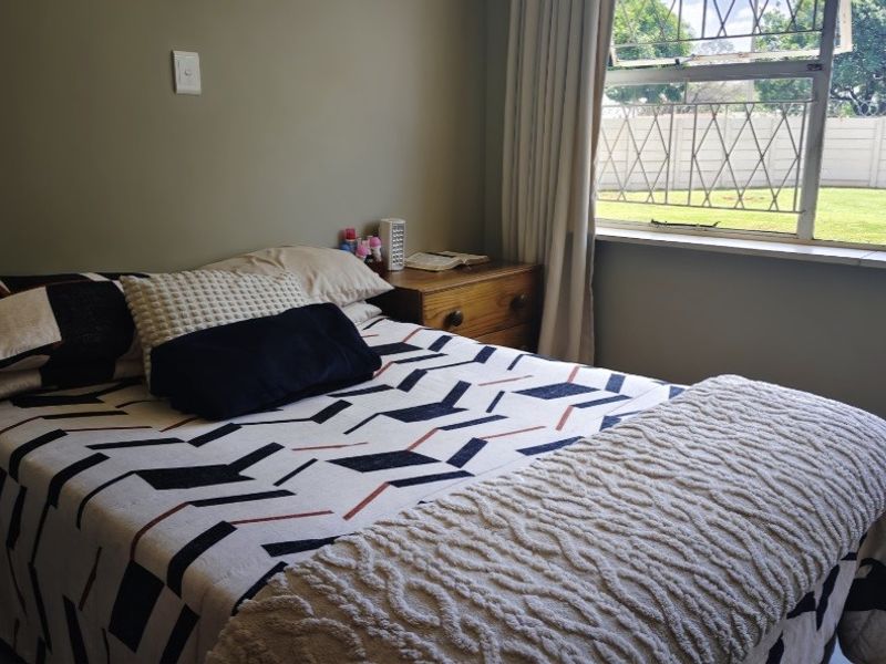A functional bedroom featuring tiled flooring, neutral wall tones, and a window fitted with security bars overlooking the garden.