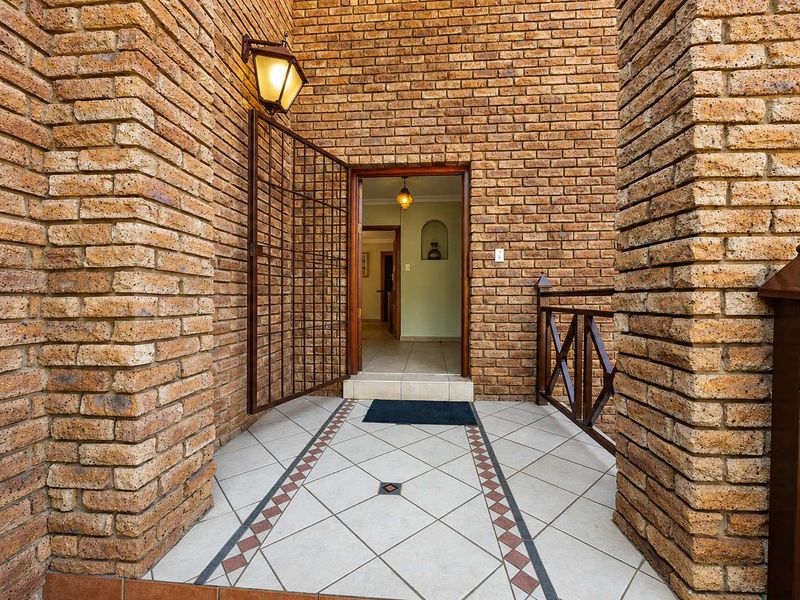 A welcoming entrance featuring exposed brick walls, decorative tiled flooring, and a secure metal gate leading into the home.