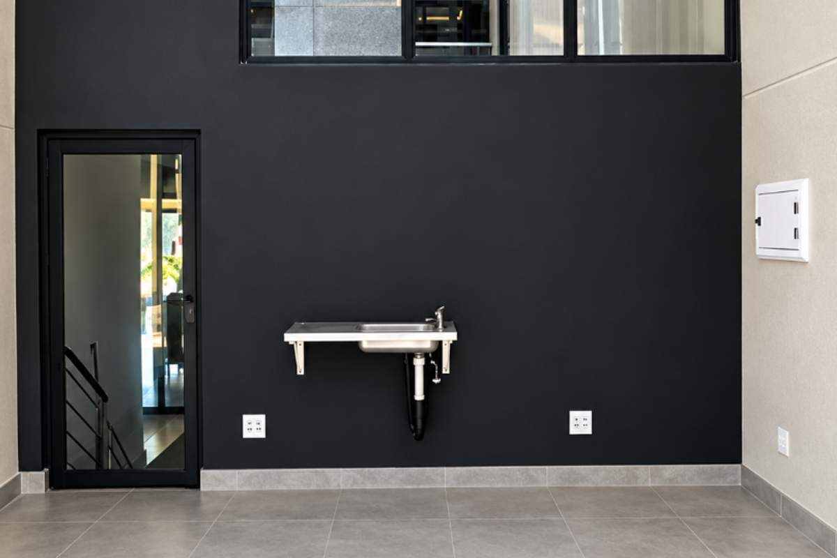 A clean, modern utility space featuring large black-framed windows, tiled flooring, and a functional wall-mounted stainless steel sink.