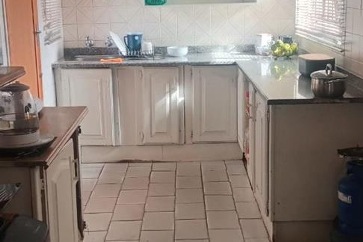 A functional kitchen featuring tiled flooring, white cabinetry, and granite-look countertops with integrated sink and tiled splashback.