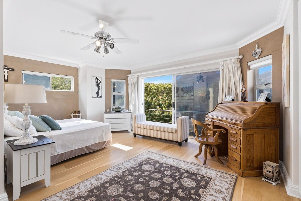 Spacious bedroom featuring hardwood flooring, crown molding, a ceiling fan, and large sliding glass doors opening to an outdoor balcony area.