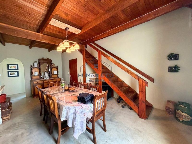 Dining area featuring exposed timber beam ceilings, concrete flooring, and a wooden staircase with a matching handrail.