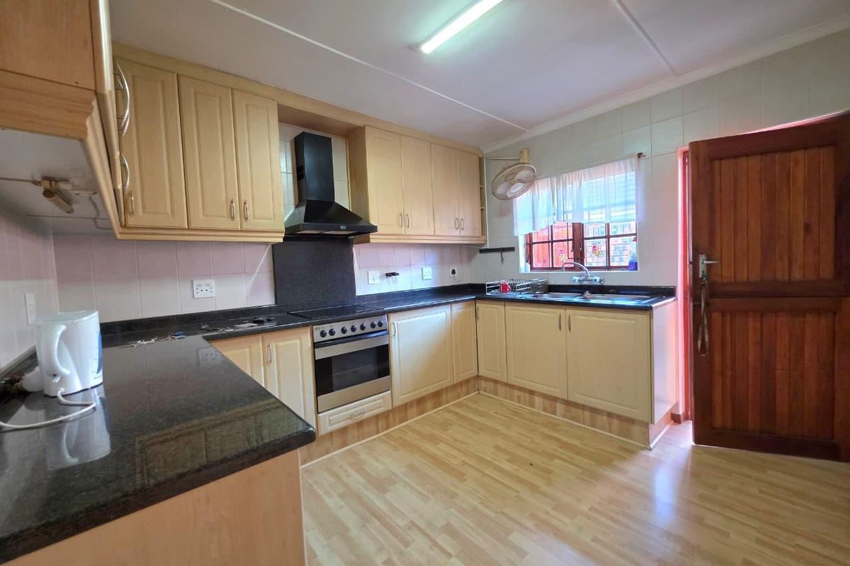 A functional kitchen featuring light wood cabinetry, dark granite countertops, a built-in oven with extractor fan, and a double sink.