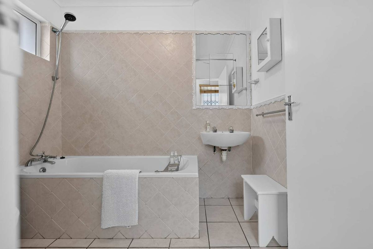 A functional bathroom featuring a bathtub with shower attachment, wall-mounted basin, and neutral tiled finishes throughout.