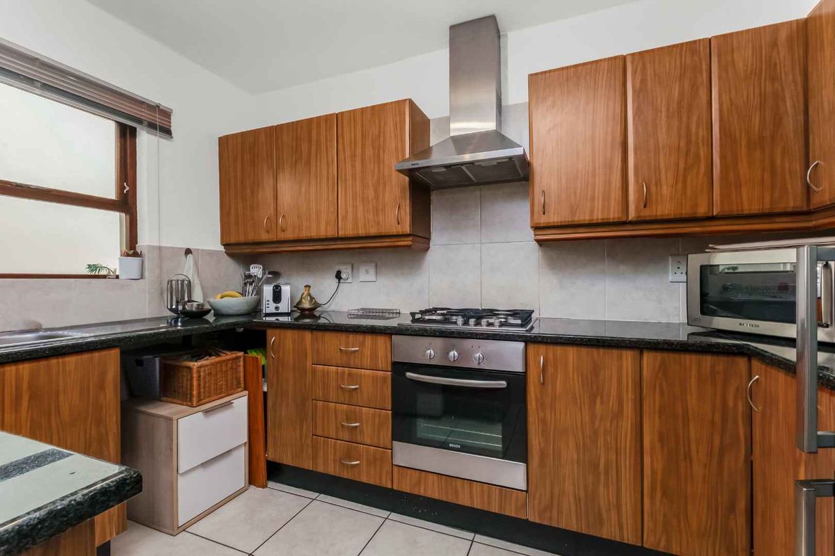 A functional kitchen featuring wood-veneer cabinetry, granite countertops, a built-in gas hob, and a stainless steel extractor fan.