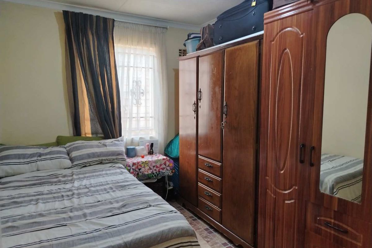 A functional bedroom featuring tiled flooring, a window with security bars, and built-in wooden wardrobe storage.