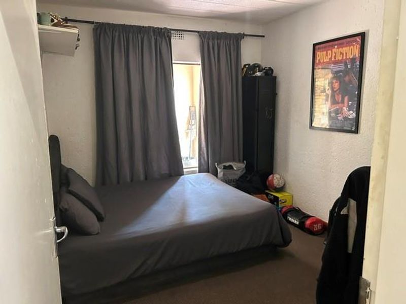 A standard bedroom featuring a window with curtains and a ventilation grille, providing a functional living space.