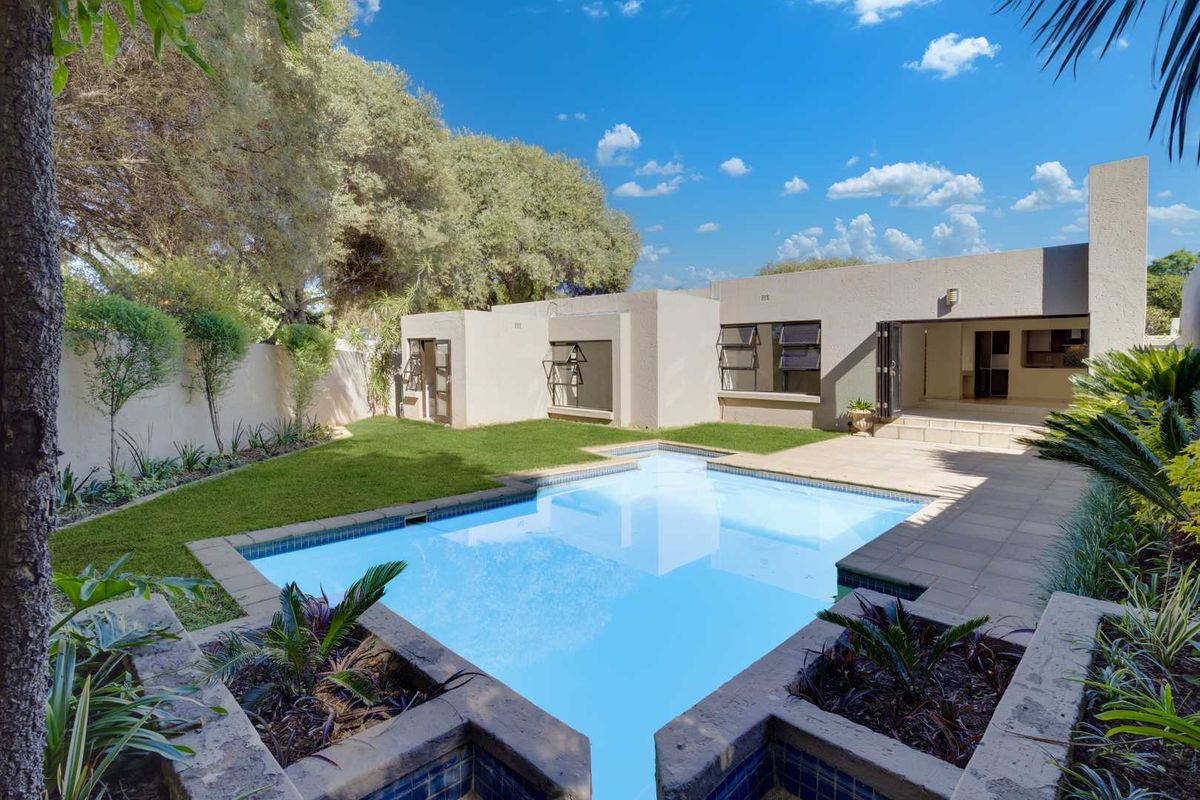 Rear exterior view featuring a swimming pool, paved patio area, landscaped garden with raised beds, and bi-fold doors leading into the home.