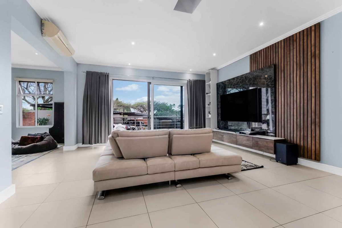 Spacious living room featuring tiled floors, a modern timber-slat feature wall with integrated media cabinetry, and large sliding doors leading to the balcony.