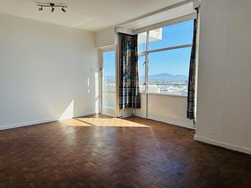 An empty living room featuring original parquet flooring, large windows with expansive mountain views, and direct access to a balcony.