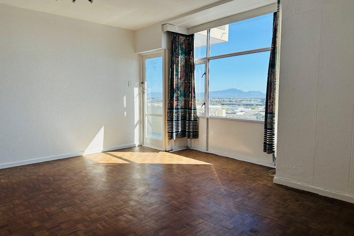 An empty living room featuring original parquet flooring, large windows with expansive mountain views, and direct access to a balcony.