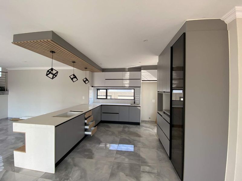 Modern kitchen featuring sleek grey cabinetry, quartz countertops, an integrated oven, and a stylish slatted timber ceiling detail over the breakfast island.