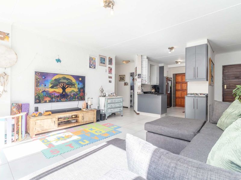 Open plan living area featuring tiled flooring, a compact kitchen with built-in cabinetry, and a breakfast counter, flowing into the main lounge space.