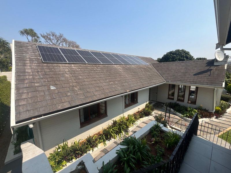 Elevated view of the rear exterior featuring a tiled roof with integrated solar panels, brick walls, and a well-maintained landscaped garden area.