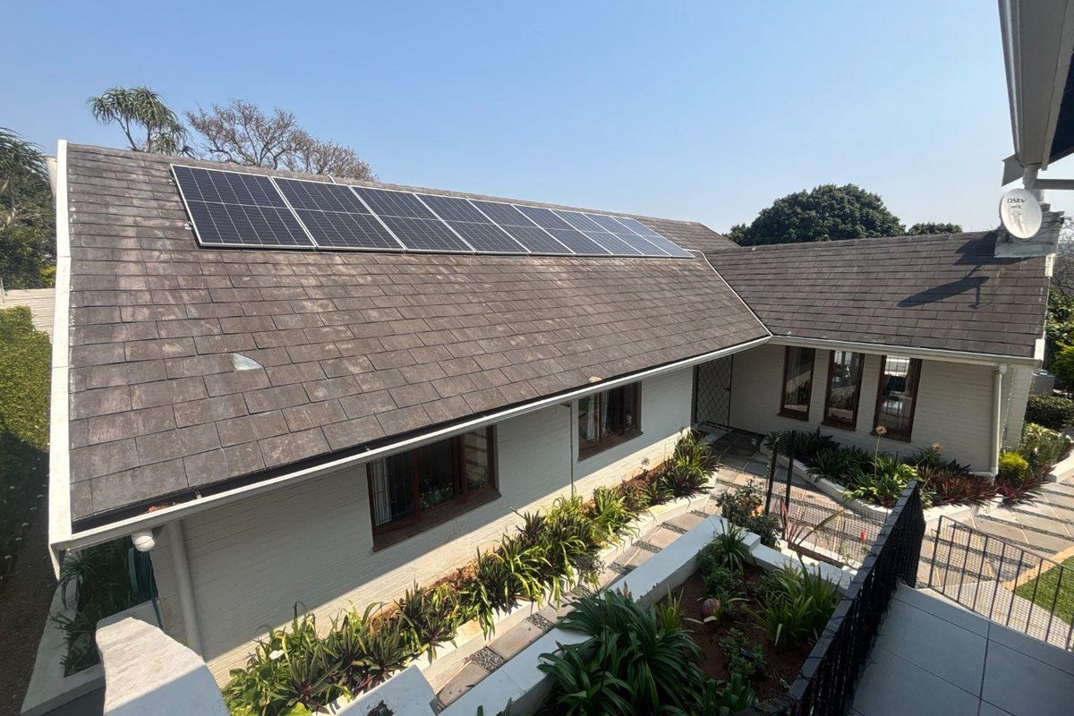 Elevated view of the rear exterior featuring a tiled roof with integrated solar panels, brick walls, and a well-maintained landscaped garden area.