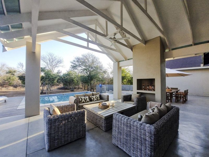 Spacious covered patio featuring a built-in fireplace, exposed timber trusses, and direct access to an outdoor swimming pool and garden area.