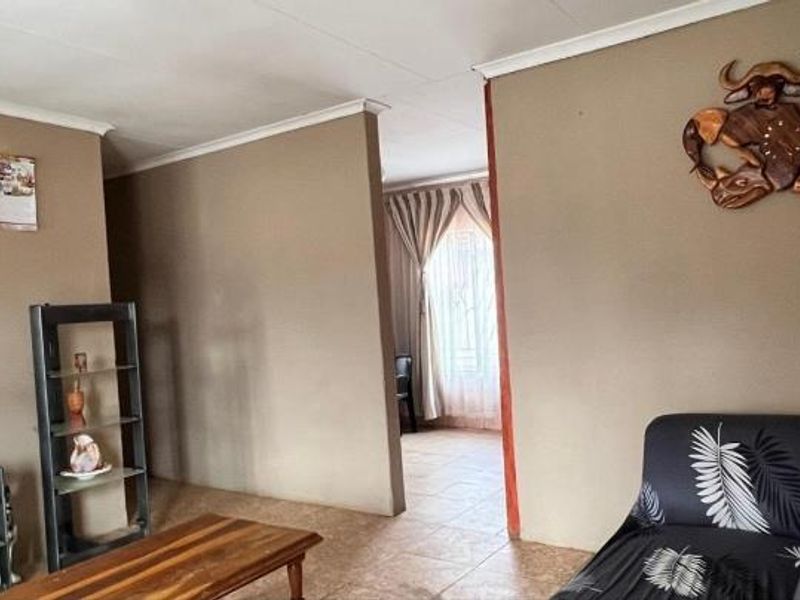 A living room area featuring tiled flooring and coved ceilings, with an open transition to an adjacent space.