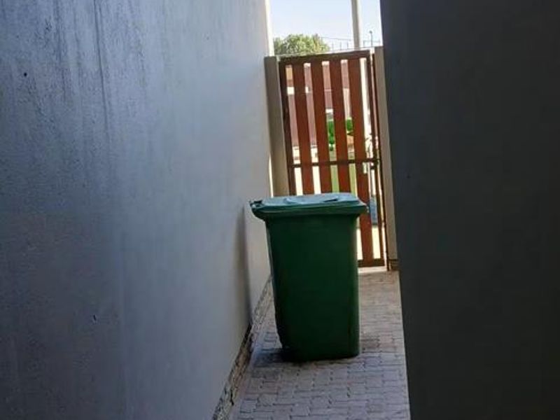 A narrow paved side passage or rear utility area featuring a timber gate and exterior wall lighting.