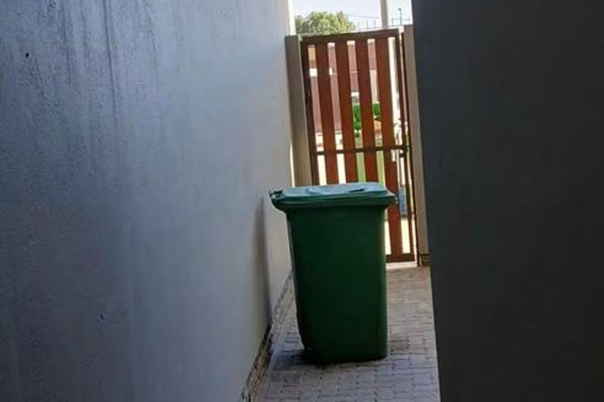 A narrow paved side passage or rear utility area featuring a timber gate and exterior wall lighting.