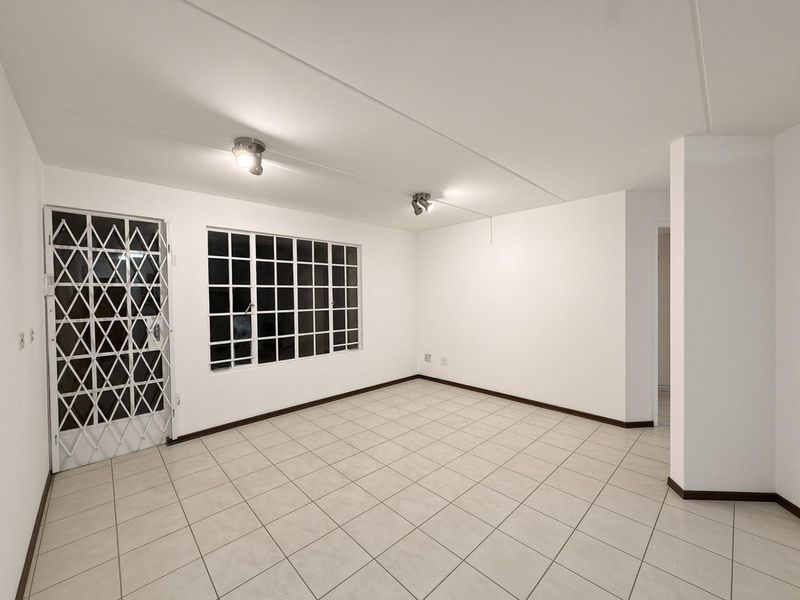 A bright, empty living room featuring neutral tiled flooring, a security gate, and large grid-pattern windows, offering a clean canvas for personalization.
