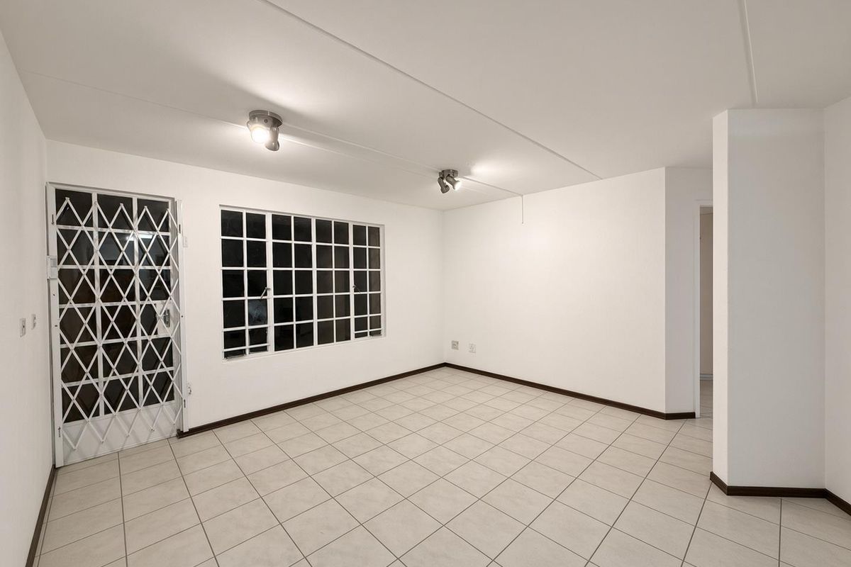 A bright, empty living room featuring neutral tiled flooring, a security gate, and large grid-pattern windows, offering a clean canvas for personalization.