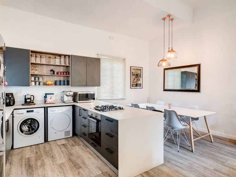 Modern open-plan kitchen and dining area featuring sleek cabinetry, gas hob, built-in oven, and integrated laundry appliances with contemporary finishes.