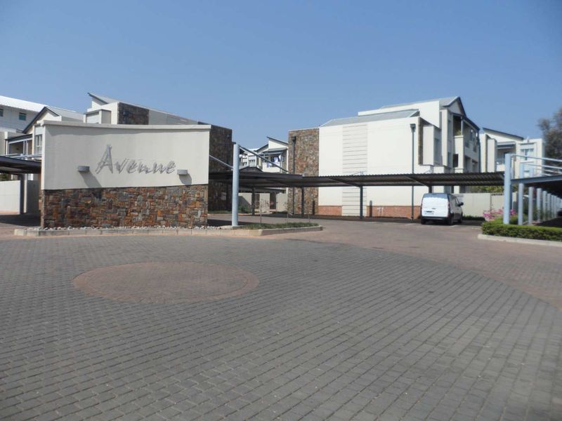 The entrance to the apartment complex features a paved driveway, stone-clad signage, and covered carport parking bays.