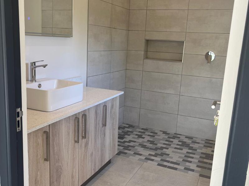 Modern bathroom featuring a wood-finish vanity with a vessel sink, a spacious walk-in shower with a built-in niche, and contemporary neutral tiling.
