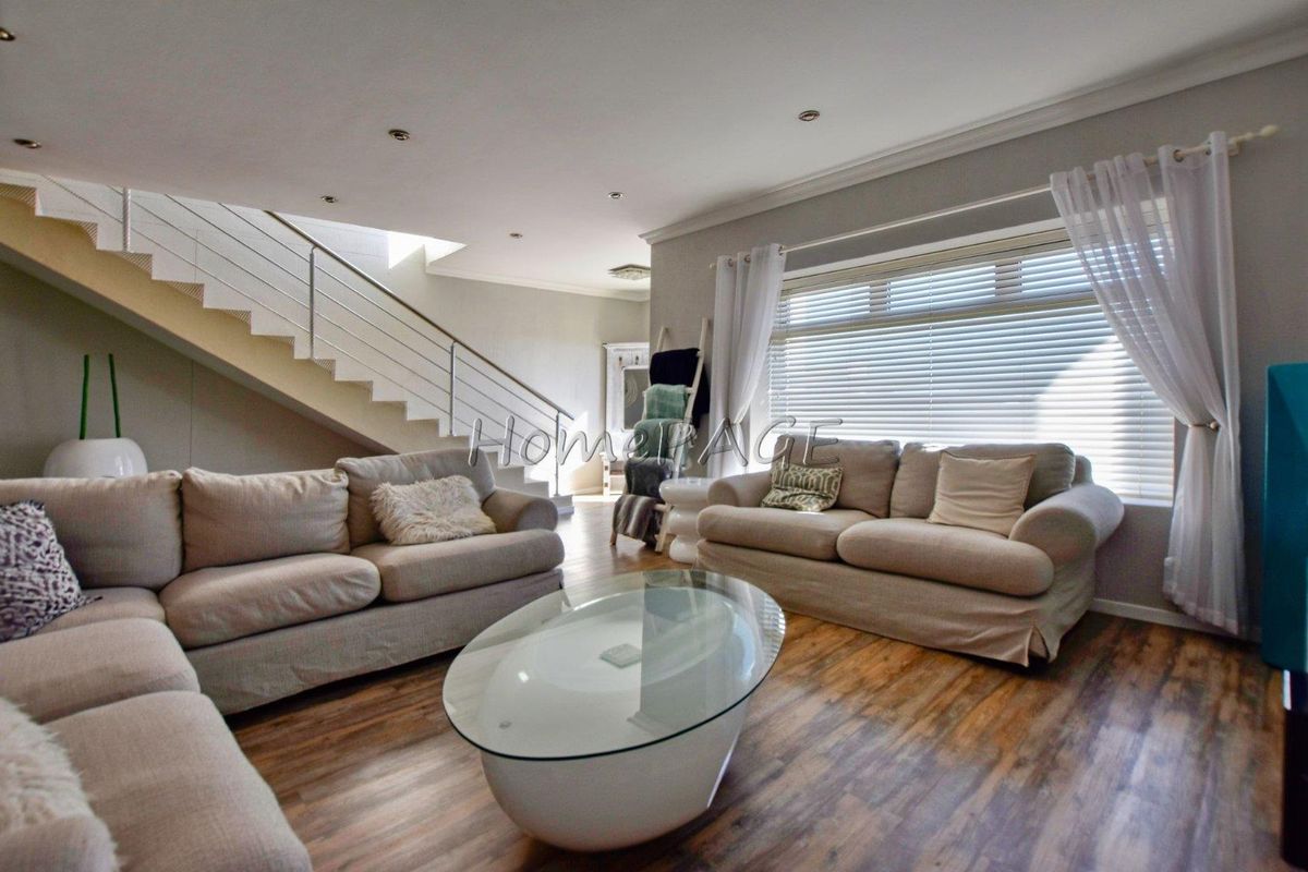 Spacious living room featuring wood-look flooring, recessed ceiling lighting, and a modern staircase with stainless steel railings.