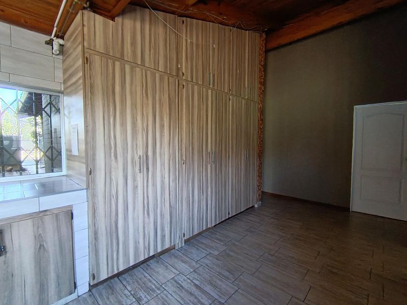 A bedroom featuring extensive built-in wooden cupboards, tiled flooring, and exposed timber ceiling beams, offering a functional space with potential for cosmetic updates.