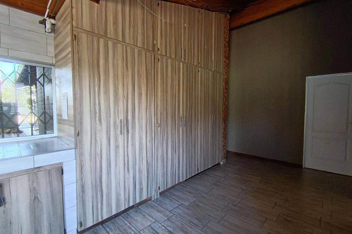A bedroom featuring extensive built-in wooden cupboards, tiled flooring, and exposed timber ceiling beams, offering a functional space with potential for cosmetic updates.