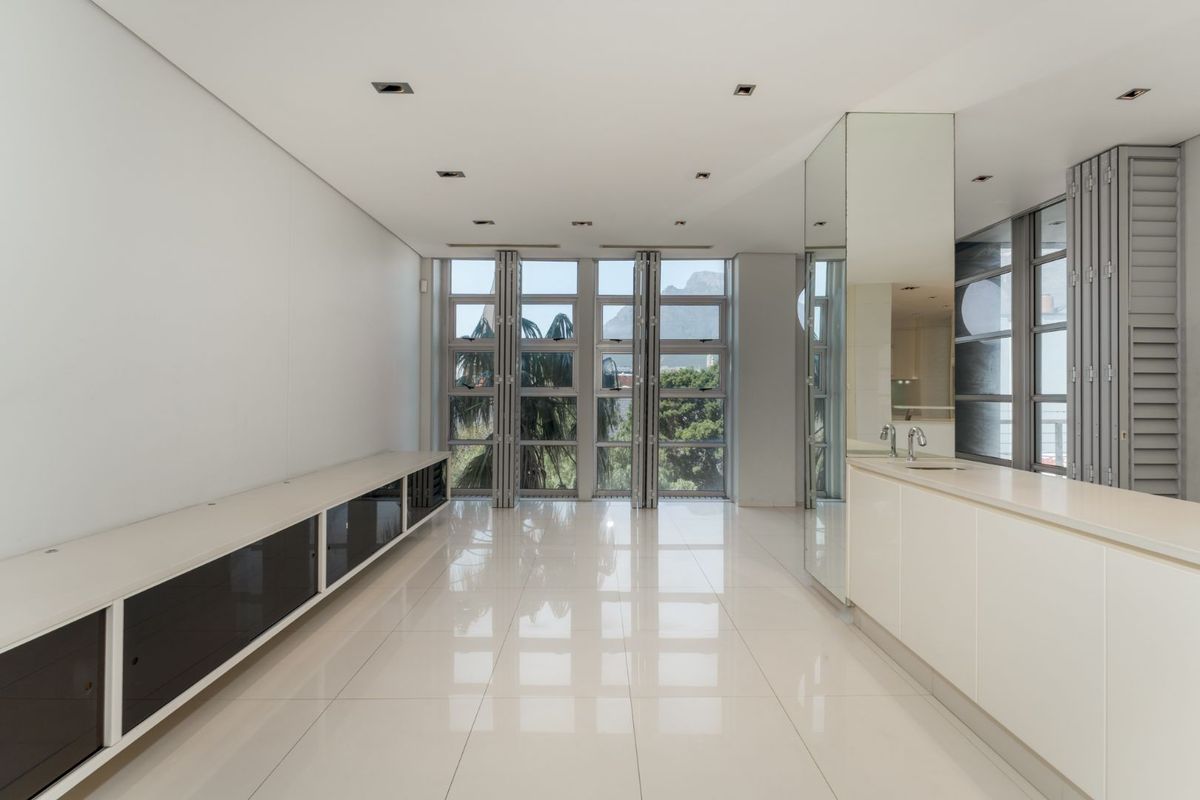 Spacious, modern living area featuring high-gloss tiled floors, built-in cabinetry, integrated sink, and large windows with folding shutters offering natural light.