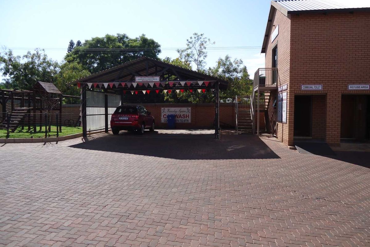 Exterior view of the apartment complex featuring a paved parking area, covered car wash bay, communal toilet facilities, and refuse area.
