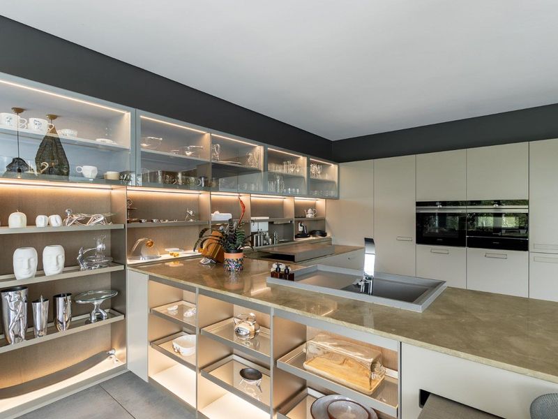 Modern, high-end kitchen featuring sleek built-in cabinetry, stone countertops, integrated sink, and professional-grade double ovens with ambient under-cabinet lighting.